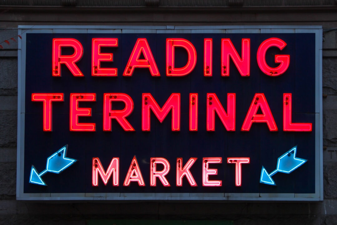 A red and blue neon sign that says "Reading Terminal Market" with two arrows