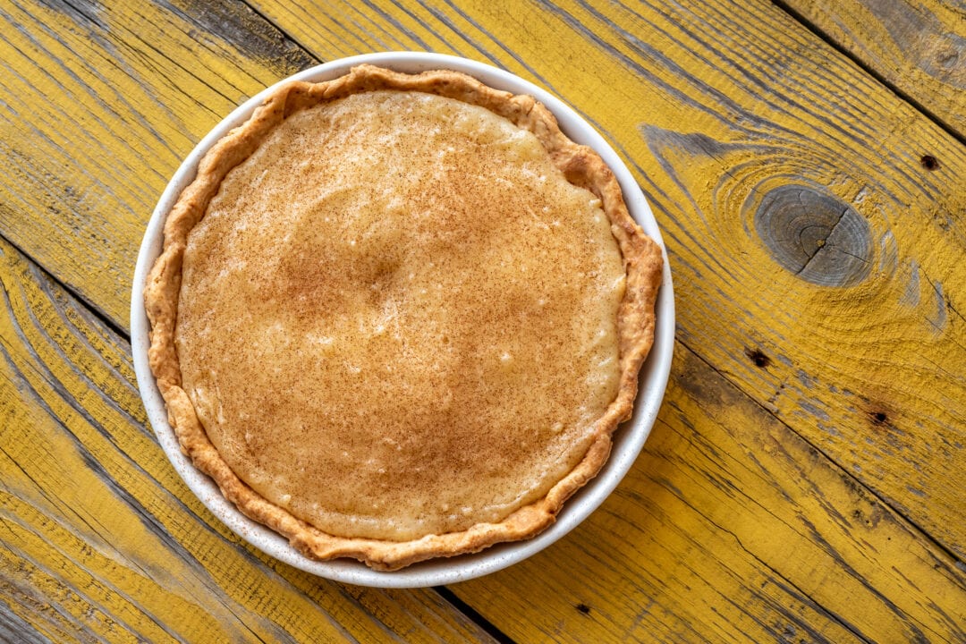 a sugar pie in a white pie plate sits on a yellow wooden table