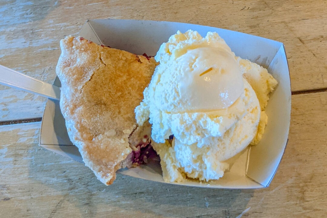 a slice of pie and a scoop of vanilla ice cream sit on a wooden table