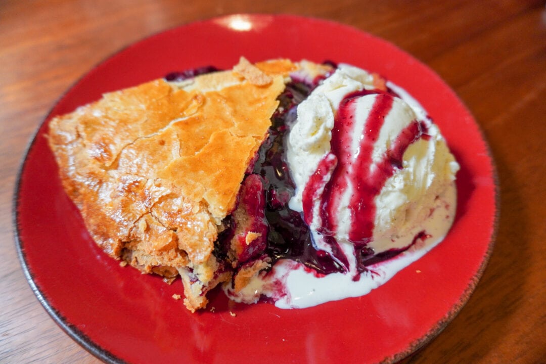 a piece of berry pie with ice cream on a red plate on a wooden table