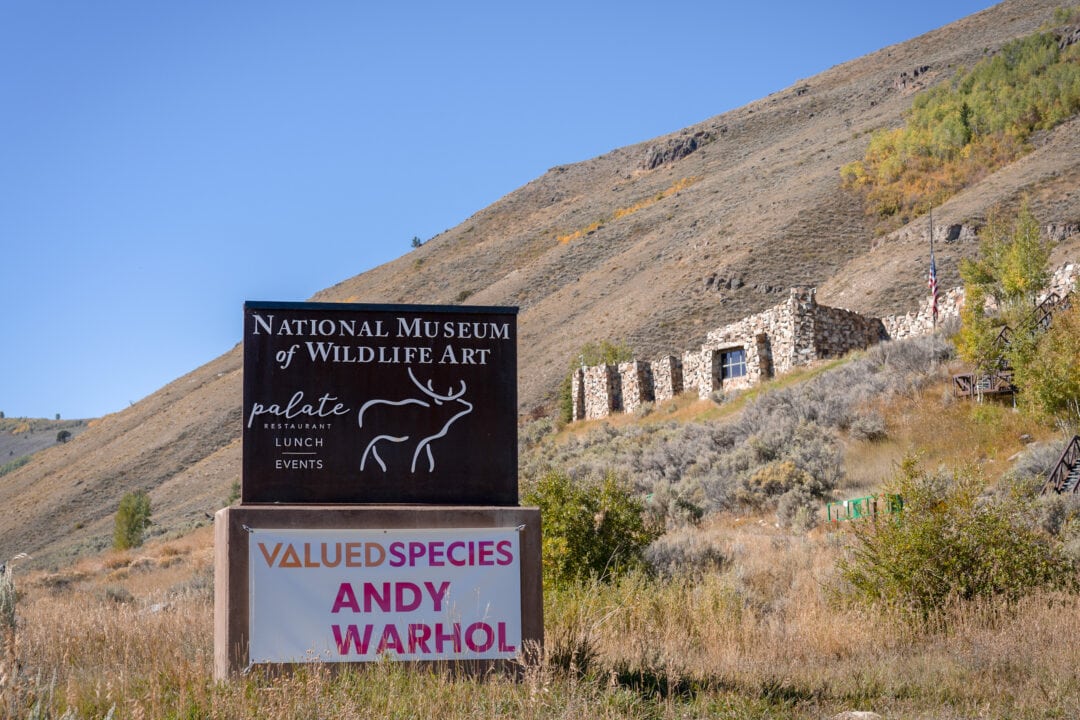 a small stone structure sits on a hillside against a blue sky with a sign for the national museum of wildlife art