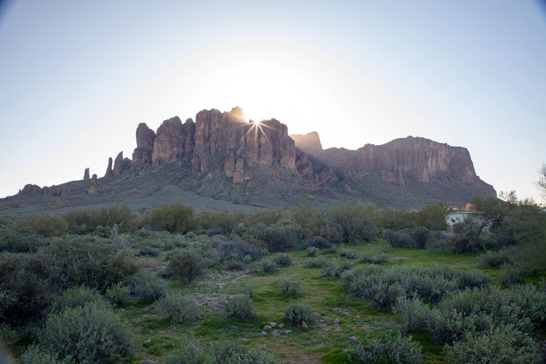 a red rock formation in front of green grassland and blue sky