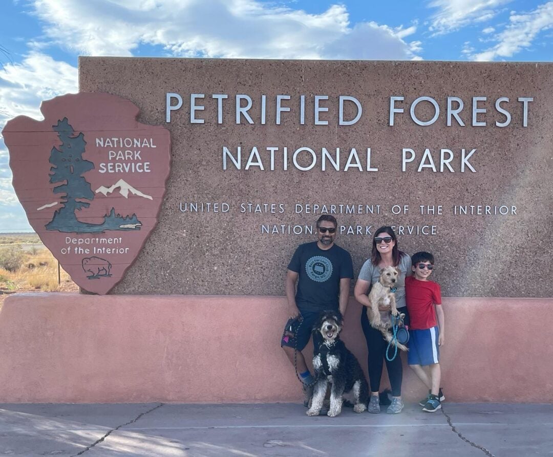 A family with their two dogs standing in front of the entrance sign for Petrified Forest National Park