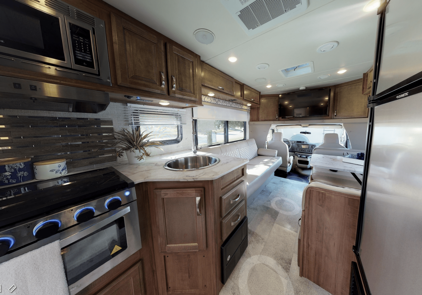 Interior of an RV with a sink, oven, microwave, fridge, dining area, and driver's cab featured 
