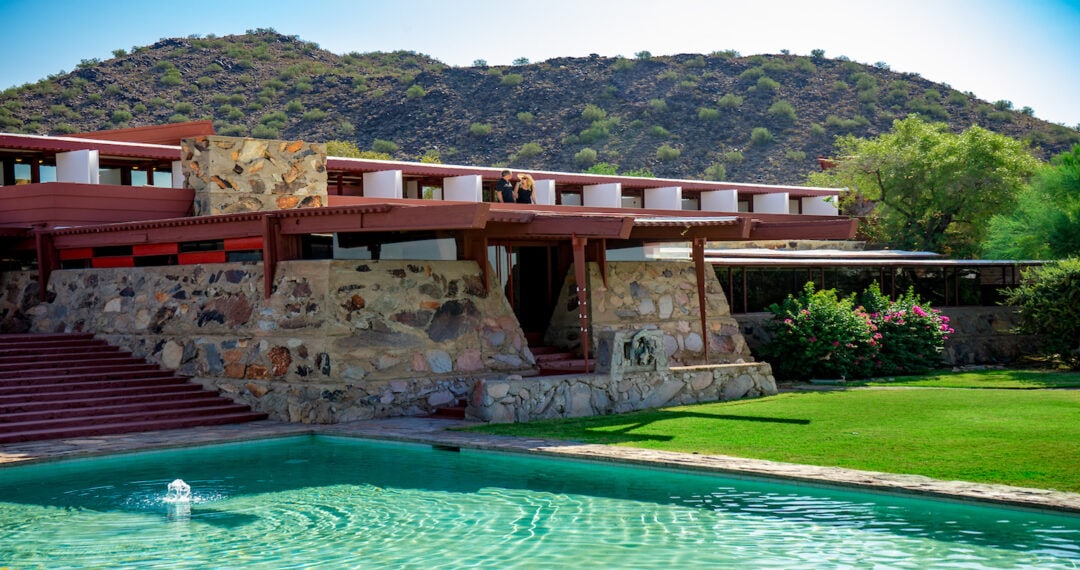 the exterior of the stone and wood taliesin west with mountains in the background and a pool in the foreground
