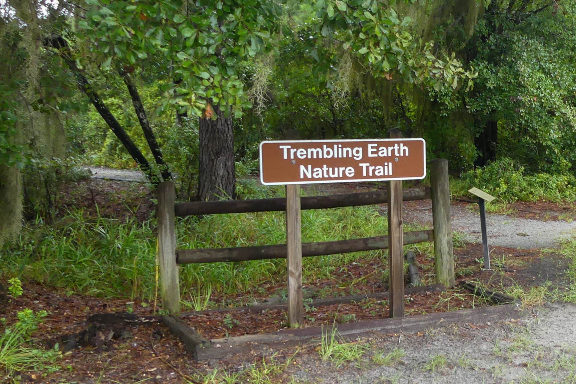 a brown and white sign says "trembling earth nature trail" surrounded by greenery