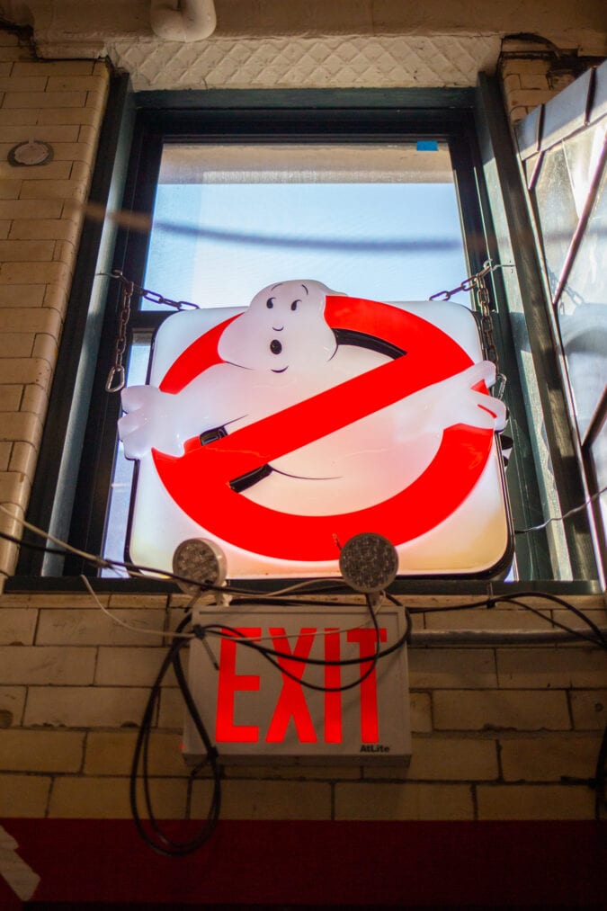 a red and white ghostbusters sign hangs in a window above an exit sign