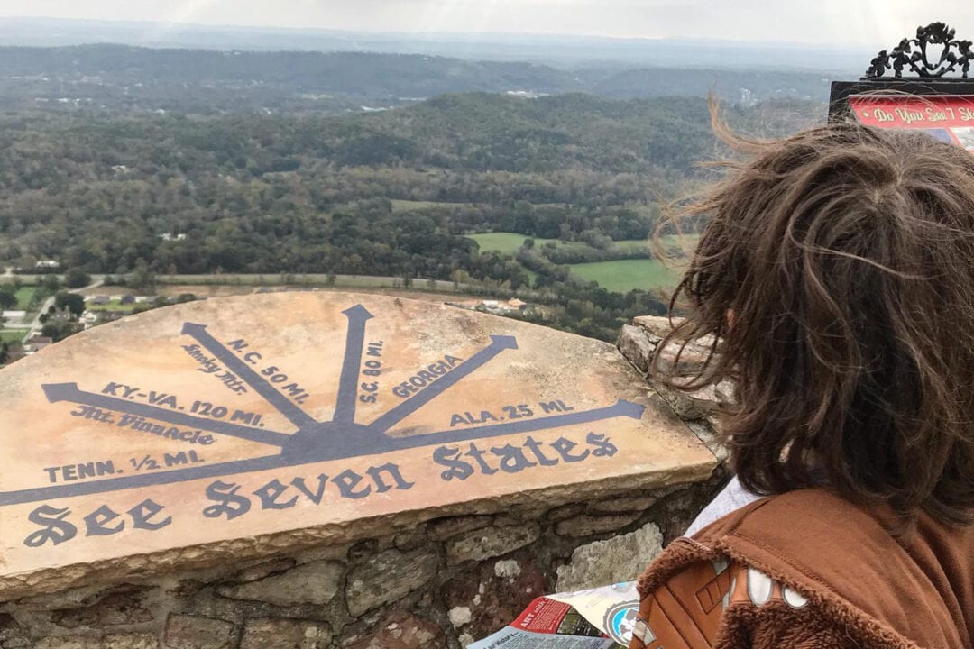 a kid stands at a mountain lookout with directional signage pointing to seven states