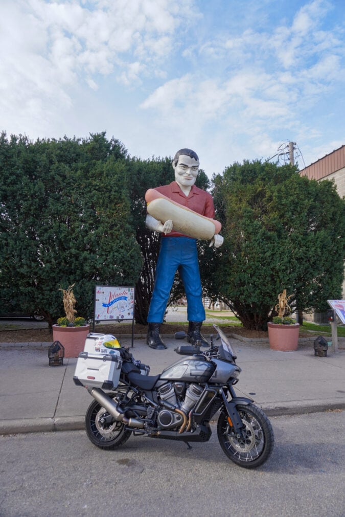 A motorcycle parked in front of a large fiberglass statue of a man holding a hot dog