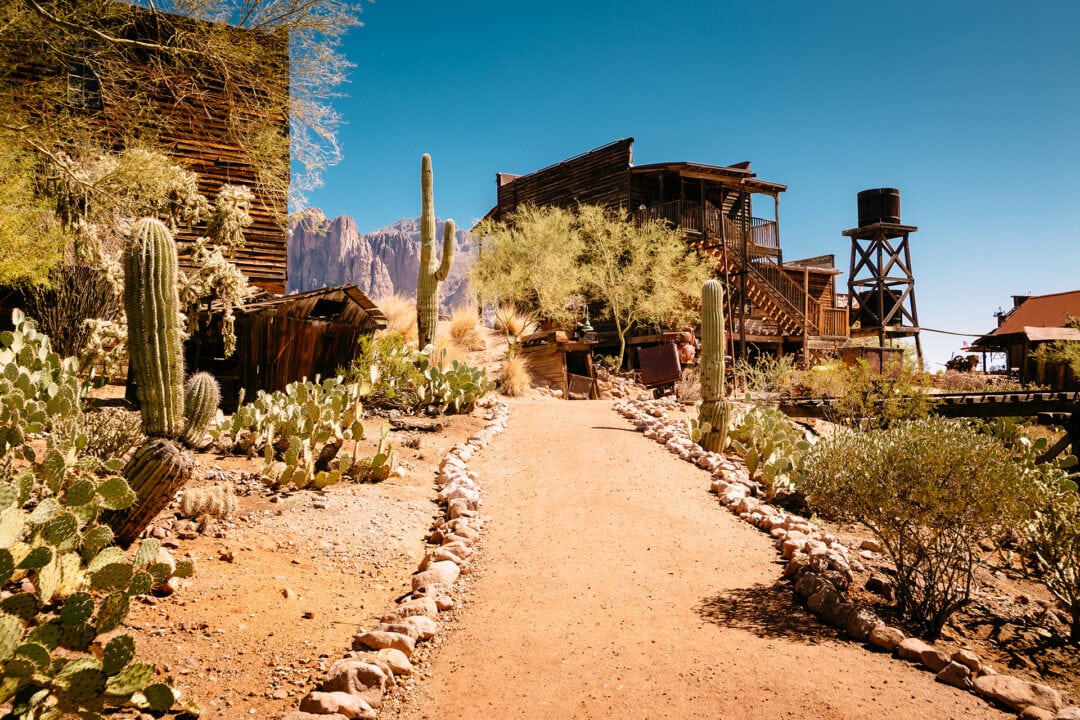 a old mining town with wooden buildings in the desert surrounded by cacti and blue skies