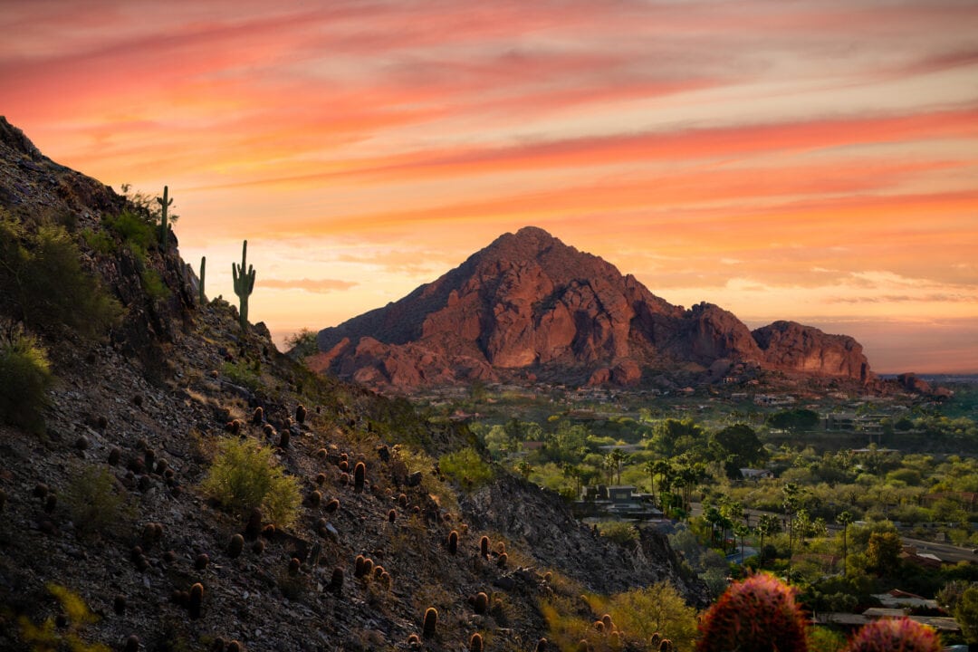 an orange and pink sunset sky over a mountain peak in the desert