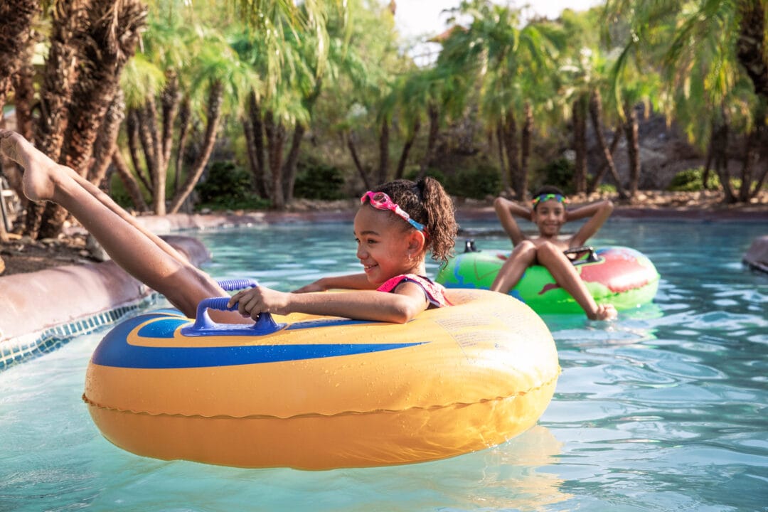 kids float on blow up tubes on a lazy river surrounded by palm trees