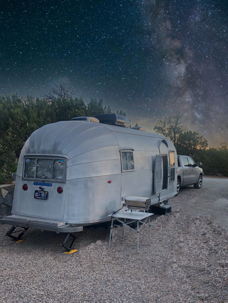 an airstream and a truck parked at a campsite under a sky of stars