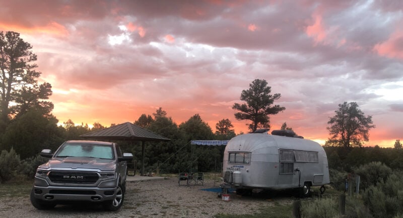 a gray truck and a silver airstream are parked under a pink sky at a campsite