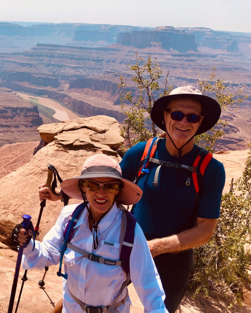 Two people in hiking gear with a red rock cliff backdrop