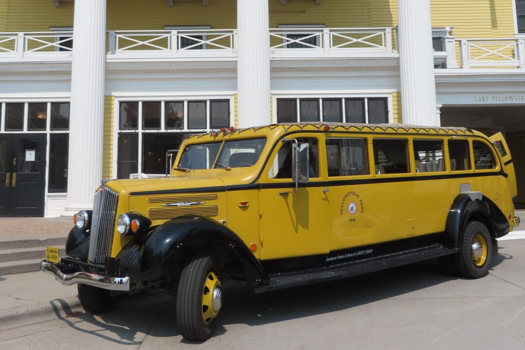 a yellow and black stretch tour vehicle with several windows sits parked outside of a yellow and white hotel entrance