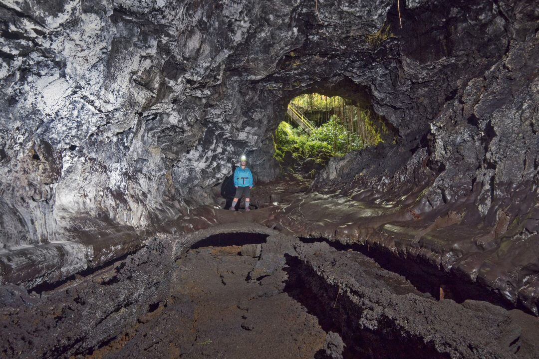 a person with a head lamp stands in a large rock cave