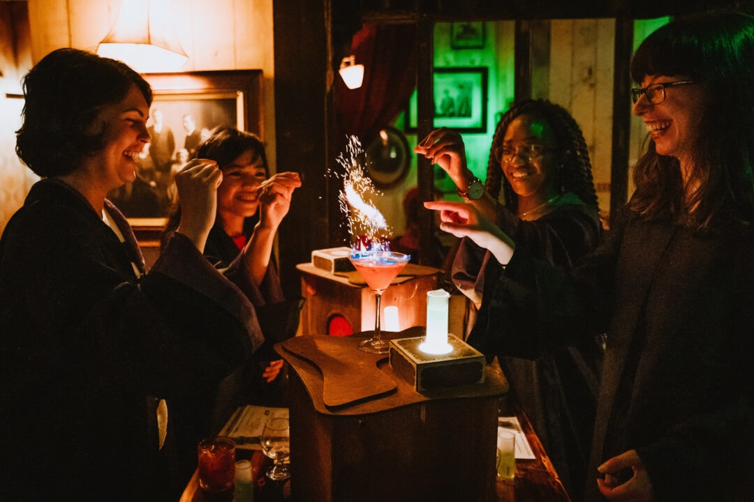 four people stand around a cocktail that looks like it's on fire