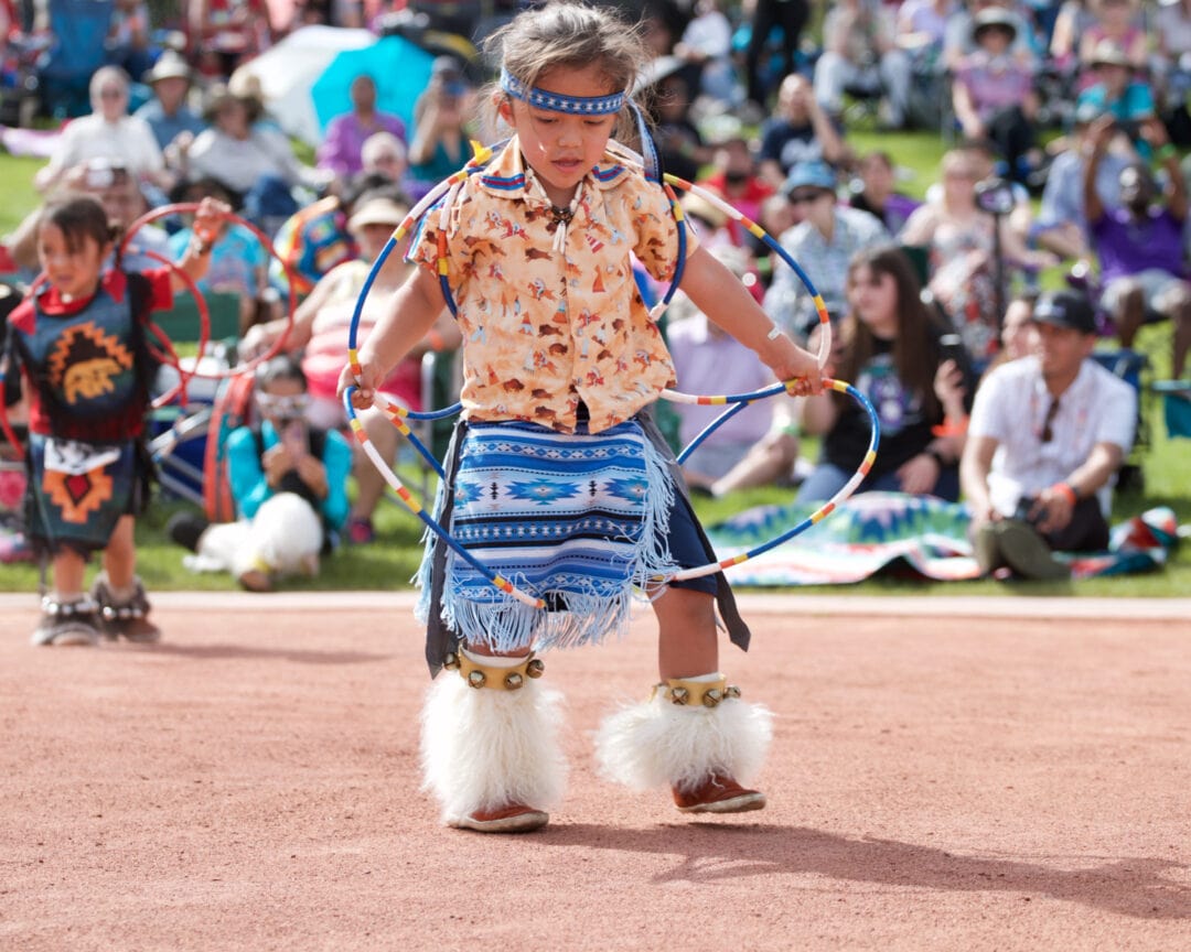 a small native american boy in regalia spins hoops in front of a crowd
