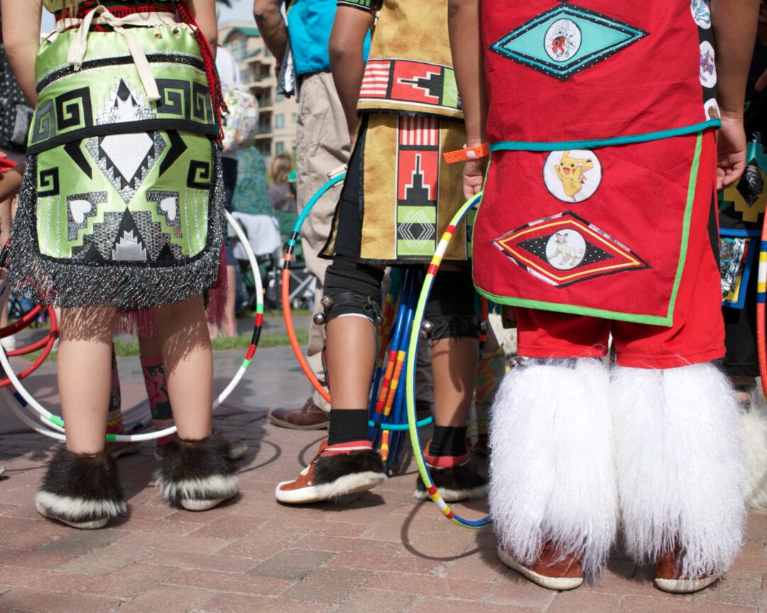 the feet of three people dressed in native regalia holding hoops