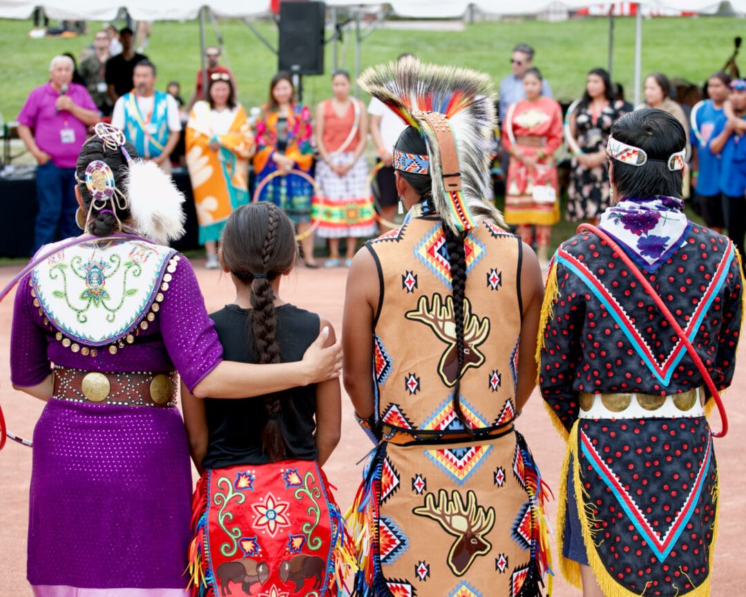 four people in native american regalia stand and face another line of people