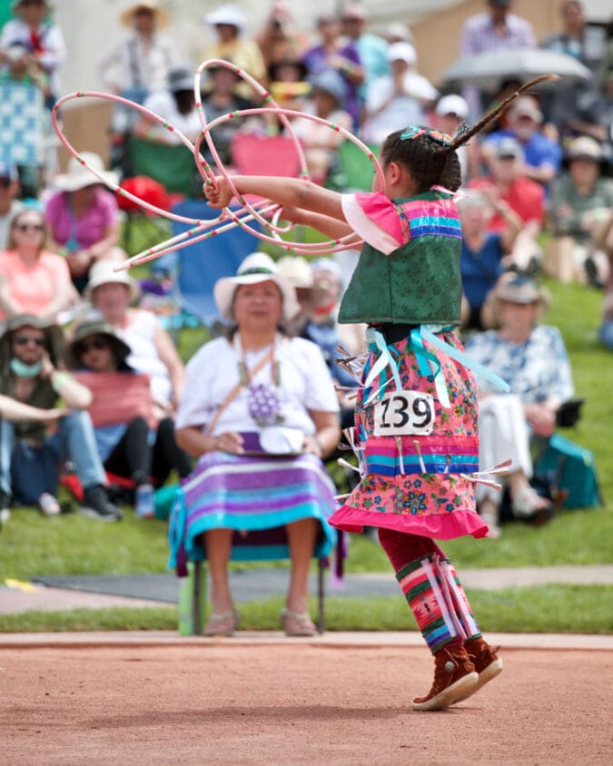 a girl in native regalia spins several hoops in front of a crowd