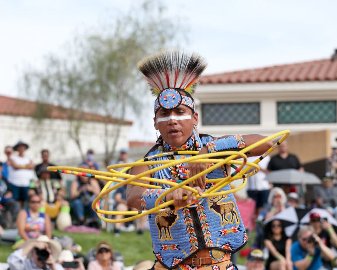 a man in native american regalia spins yellow hoops in front of a crowd