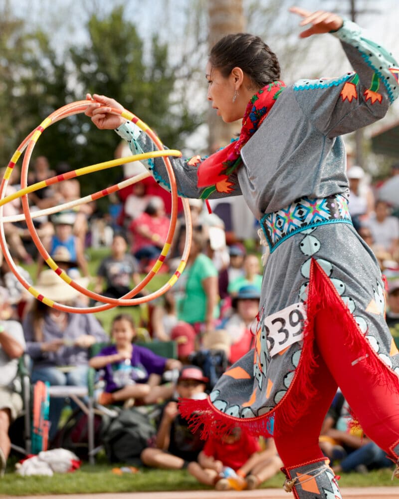 a woman in native regalia spins several hoops in front of a crowd