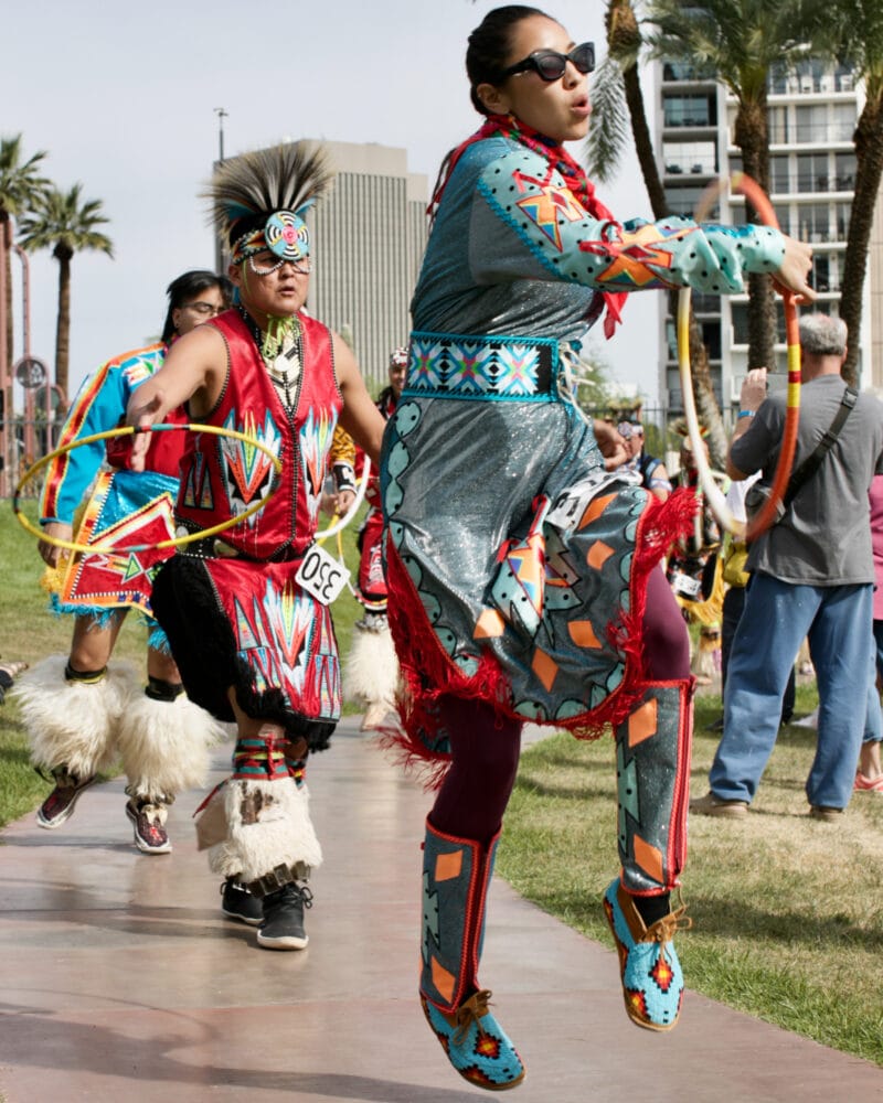a procession of three people dressed in native regalia dances in a line