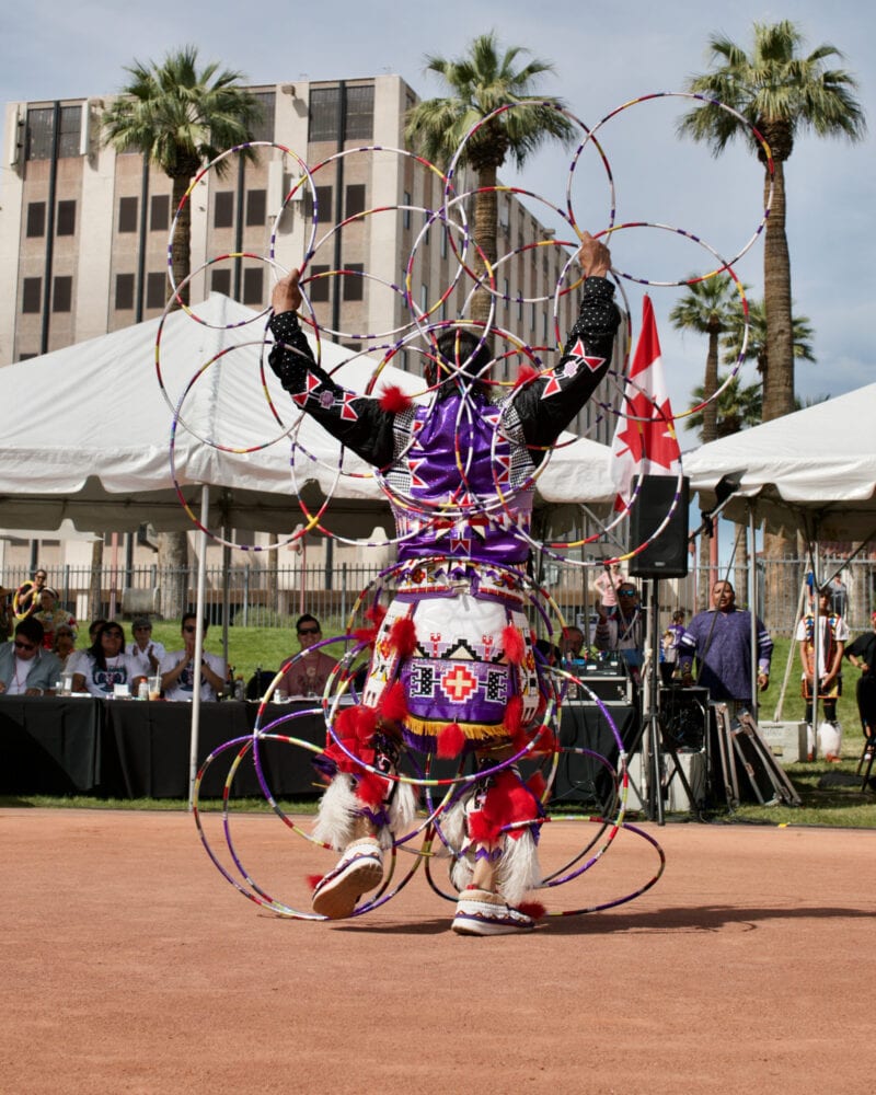a man in native american regalia balances several hoops in front of white tents