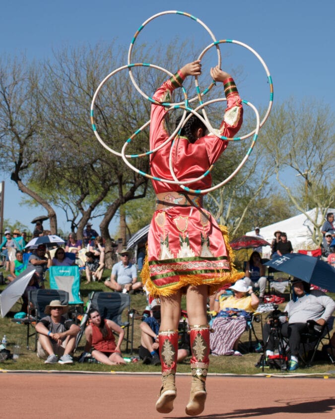 the back of a woman in native american regalia spinning hoops and dancing in front of a crowd