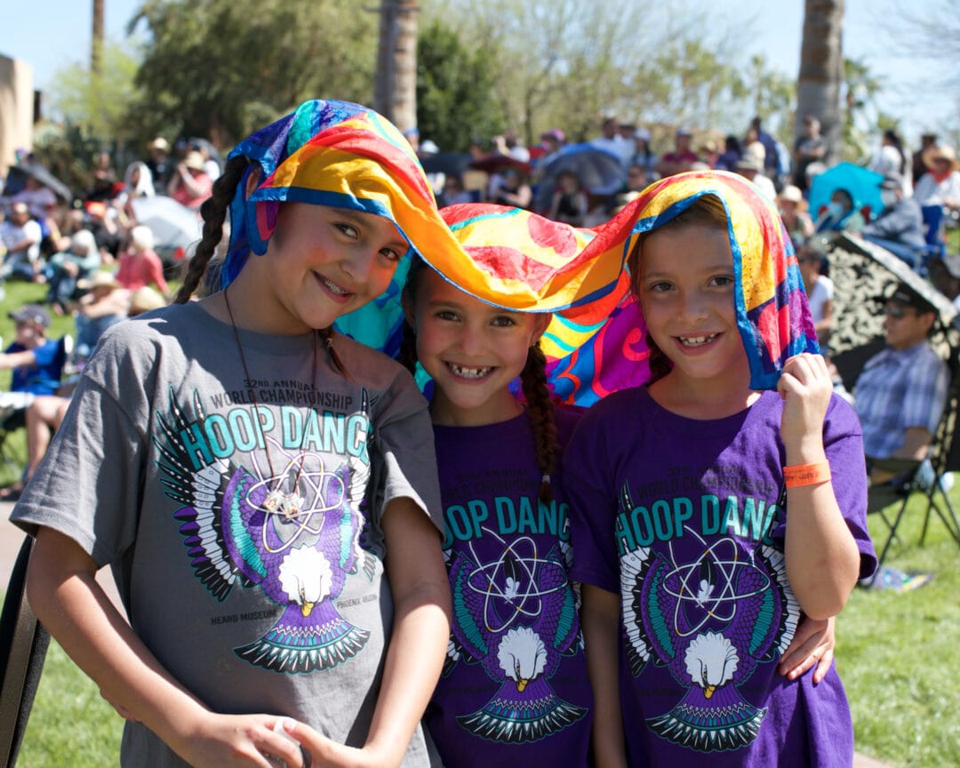 three kids wearing purple hoop dancing tshits smile under a scarf