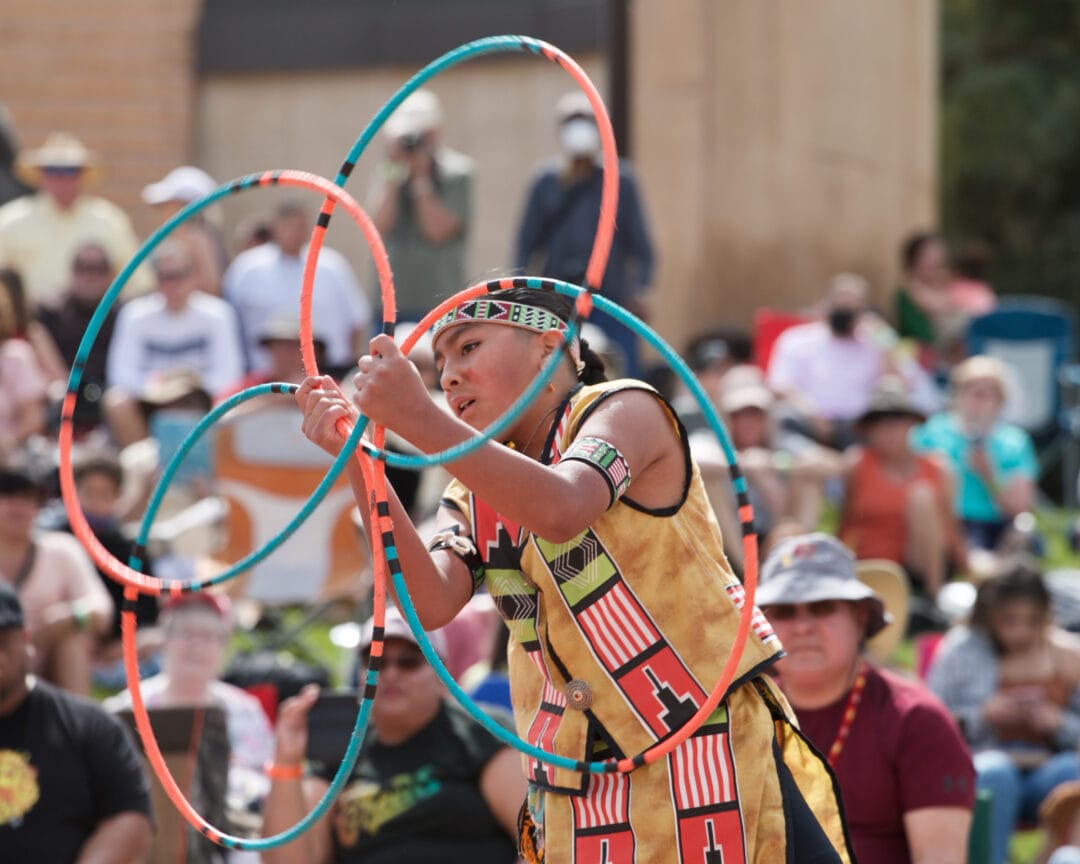 a boy dressed in native regalia spins two orange and teal hoops
