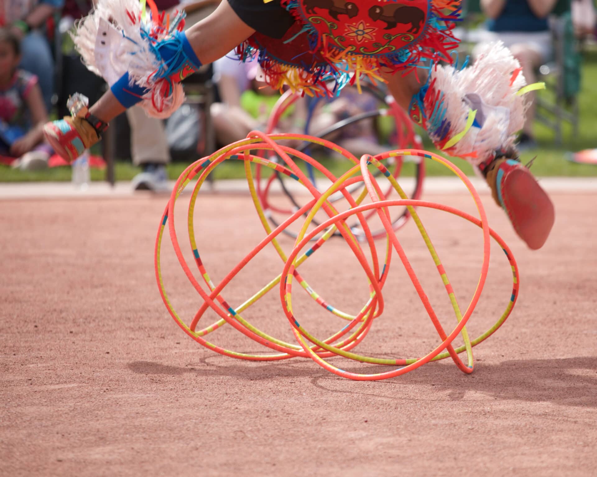 a person in native regalia jumps over a tangle of orange and yellow hoops
