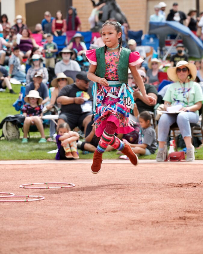 a girl in native regalia jumps in front of a crowd