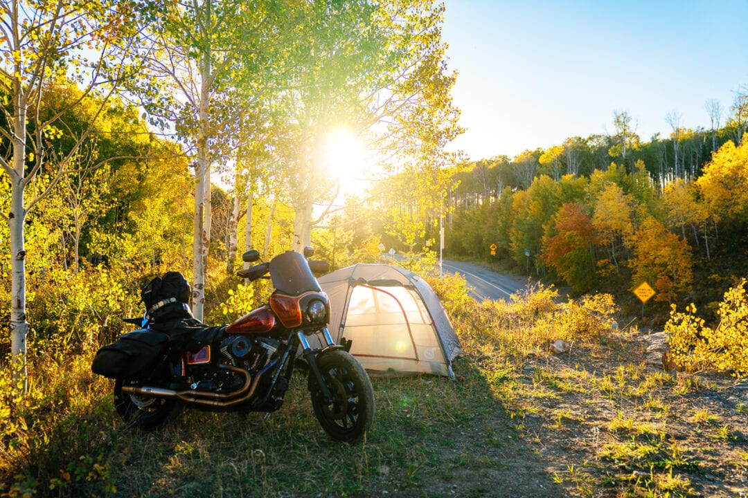 A motorcycle parked next to a tent at golden hour, surrounded by fall foliage 