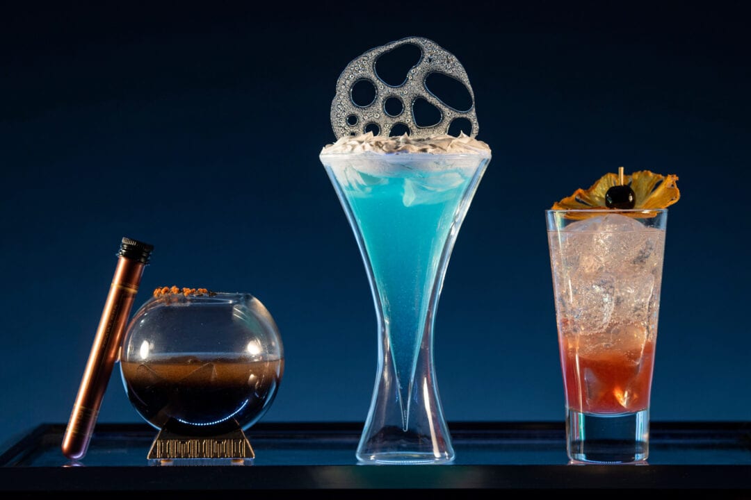 three fancy and colorful cocktails photographed against a dark blue backdrop