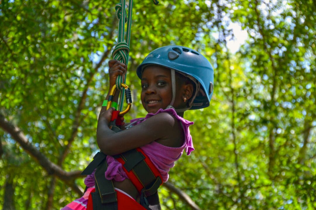 a child wearing a blue helmet climbs a tree with the help of ropes
