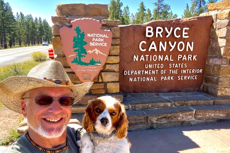 a man and his dog pose in front of the entrance sign to bryce canyon national park