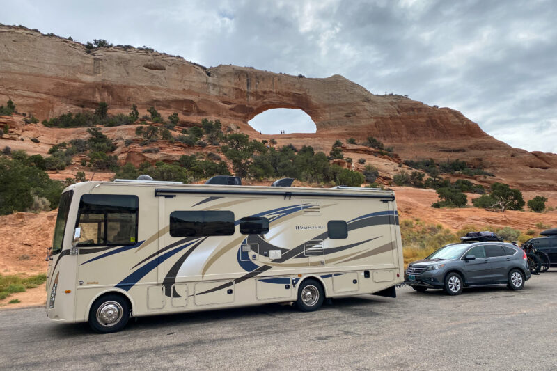 an rv and a car are parked in front of a red rock arch formation