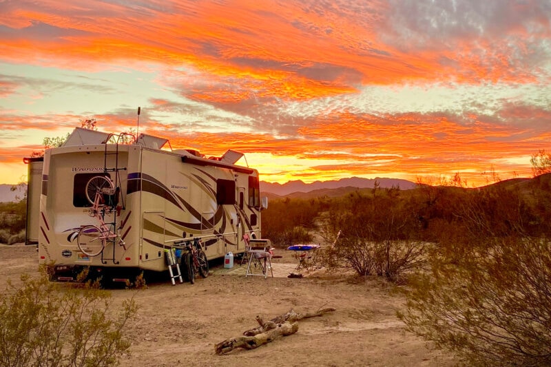 an rv is parked in the desert under an orange sunset sky
