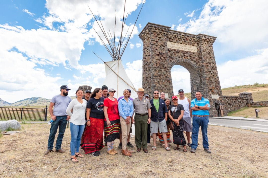 a group of people pose in front of a teepee and stone entrance to yellowstone national park