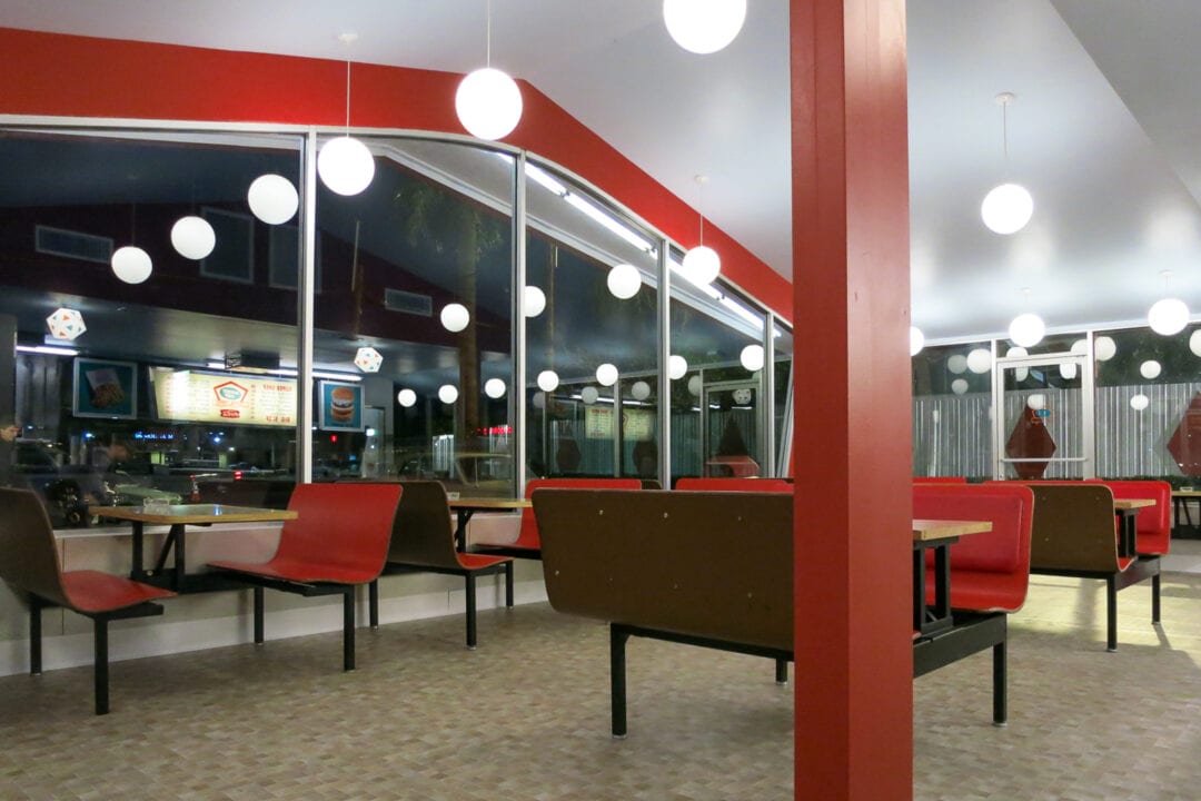 the interior of a burger restaurant with red booths and white spherical lights