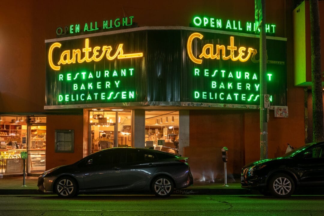 a yellow and green neon corner sign for Canter's deli lit up at night
