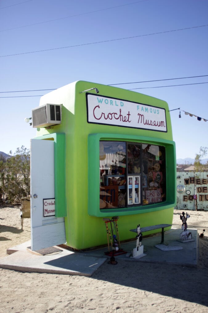 a small bright green photo processing booth with a sign that says "world famous crochet museum"