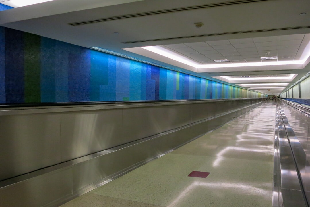 an airport corridor with a blue and green abstract mosaic stretching along the wall