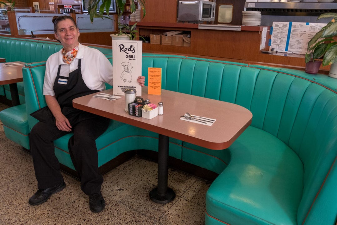 a waitress poses with a menu in a turquoise diner booth