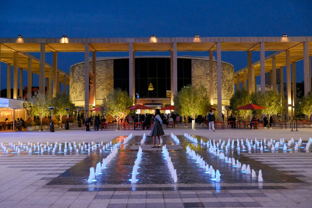 the outside plaza of the music center at night with cafe tables and a fountain