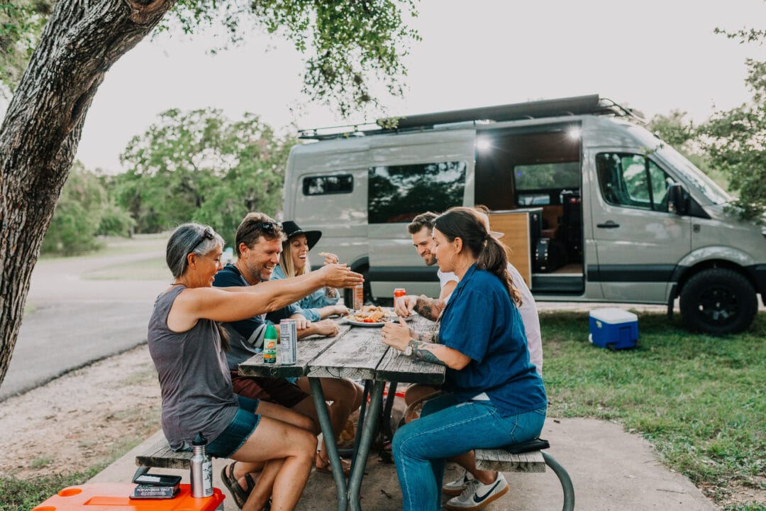A group of people sitting outside a van at a picnic table