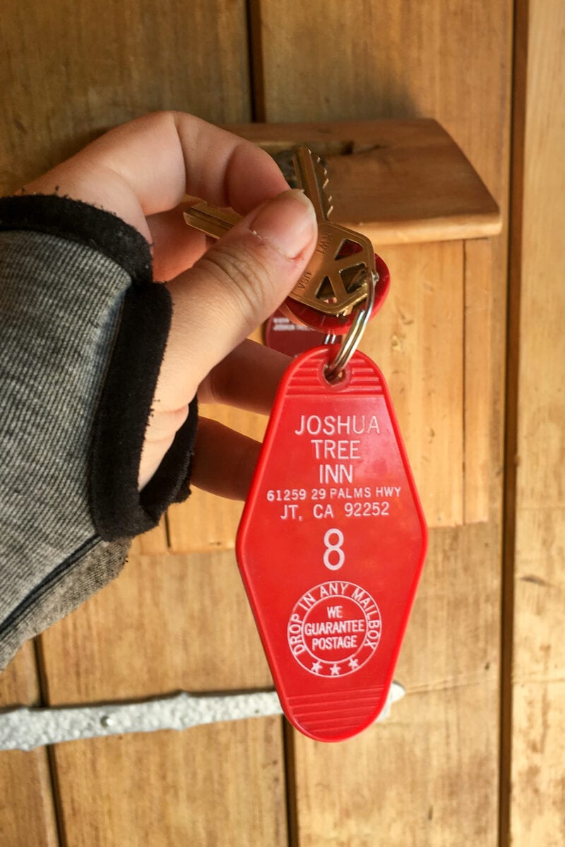 a hand holds a red plastic key tag that says "joshua tree inn room 8"